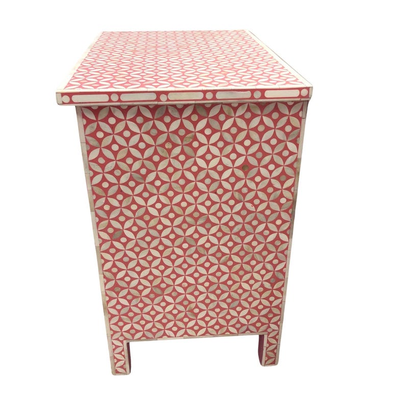 May include: A red and white patterned cabinet with a geometric design. The cabinet has a rectangular shape with four short legs. The pattern is made up of circles and petal-like shapes. The cabinet is a decorative piece of furniture.