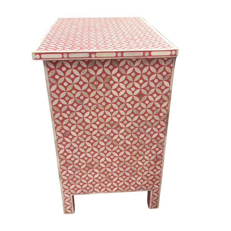 May include: A red and white patterned cabinet with a geometric design. The cabinet has a rectangular shape with four short legs. The pattern is made up of circles and flower-like shapes. The cabinet is likely made of wood.