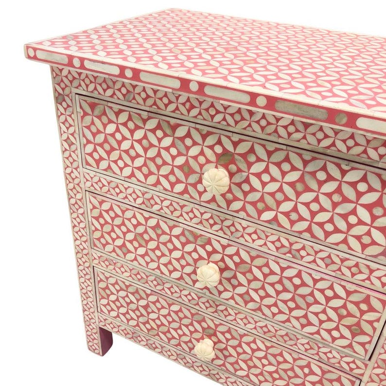 May include: A four-drawer chest of drawers with a red and white floral pattern. The chest has a rectangular shape with a flat top and decorative knobs. The pattern is repeated on the top, sides, and drawer fronts.