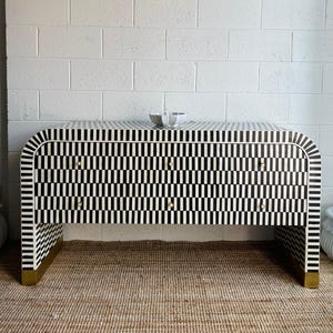 May include: A black and white patterned dresser with four drawers and brass-colored feet. The dresser has a curved front and a small bowl on top. The pattern is a repeating vertical stripe design.