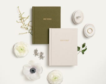 Peut inclure: Vue aérienne d'articles de mariage sur fond blanc. Deux livres de vœux, vert olive et crème, avec l'inscription dorée "HIS VOWS" et "HER VOWS". Sont également présents des boîtes à bagues, des boucles d'oreilles et des fleurs.