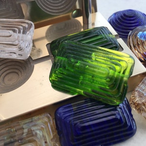 May include: Assortment of colorful glass beads with a layered, concentric design. The beads are rectangular and round in shape, with shades of green, blue, brown, and clear.