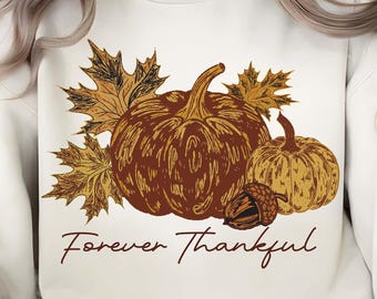 Könnte beinhalten: Cremefarbenes Sweatshirt mit einem herbstlichen Motiv. Das Design umfasst zwei Kürbisse, Herbstblätter und eine Eichel in Braun- und Gelbtönen. Die Worte "Forever Thankful" sind in einer Schreibschrift unter der Illustration geschrieben.