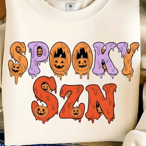 Pode incluir: Camisola creme com as palavras "SPOOKY SZN" em letras gotejantes laranja e roxas. Cada letra tem uma cara de abóbora. Um design divertido e festivo para o Halloween.
