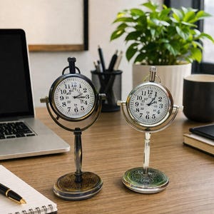 May include: Two antique-style desk clocks with white faces and black Roman numerals. The clocks are in a stand with a circular base. One clock has a black finish, and the other has a silver finish. A laptop, notepad, and pen are also on the desk.
