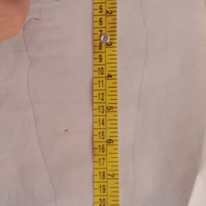 May include: A yellow measuring tape is placed next to a traced outline of a foot on white paper. The tape shows measurements in inches, with the foot outline measuring approximately 10 inches in length. The image is taken from above.