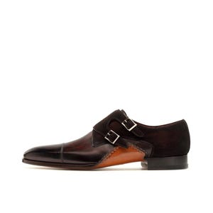 May include: A brown leather double monk strap shoe with a black toe cap and two silver buckles. The shoe features a suede panel and a contrasting tan leather section.