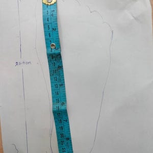 May include: A blue measuring tape is placed next to a traced foot outline on white paper. The foot outline measures 23.4 cm in length and 10.5 cm in width. The measuring tape shows the foot's length in centimeters.
