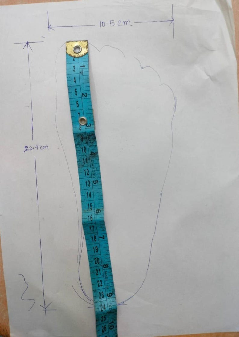 May include: A blue measuring tape is placed next to a traced foot outline on white paper. The foot outline measures 23.4 cm in length and 10.5 cm in width. The measuring tape shows the foot's length in centimeters.