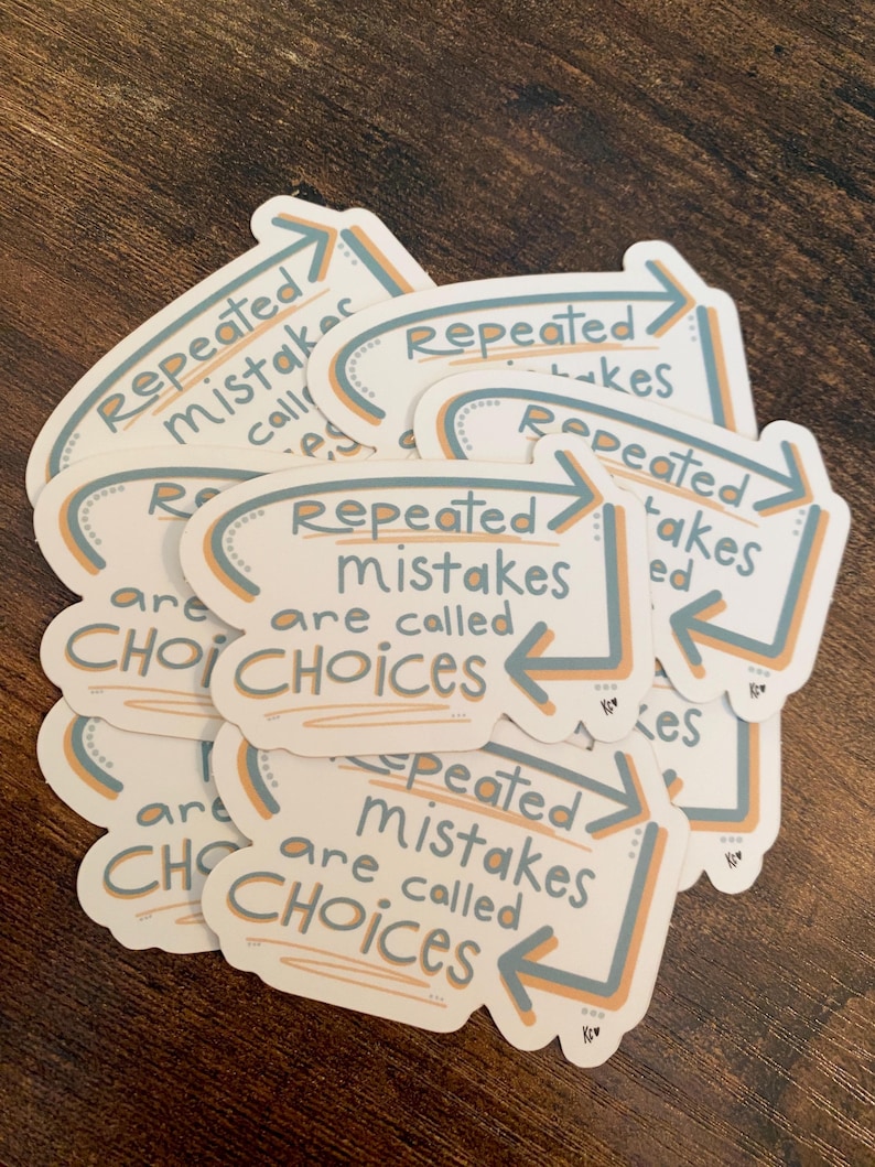 K&ouml;nnte beinhalten: Ein Stapel wei&szlig;er Aufkleber mit dem Text "Repeated mistakes are called choices" in handschriftlicher Schrift. Die Aufkleber haben ein hellblaues und orangefarbenes Pfeildesign.