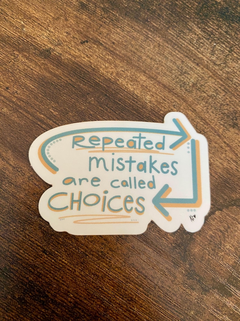 K&ouml;nnte beinhalten: Ein wei&szlig;er Aufkleber mit dem Text "Repeated mistakes are called CHOICES" in T&uuml;rkis und Orange. Der Text befindet sich in einer wei&szlig;en Form mit t&uuml;rkisfarbenen und orangefarbenen Pfeilen und Akzenten. Der Aufkleber befindet sich auf einer braunen Holzoberfl&auml;che.