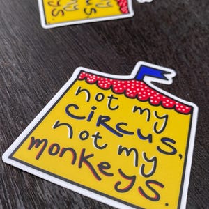 May include: Two yellow stickers with the text "not my circus, not my monkeys" in a playful font. The stickers have a tent-like design with a red and white polka-dot border and a blue ribbon.