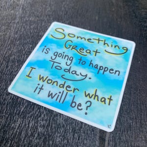 May include: A square sticker with a sky-blue background and white clouds. The sticker has the handwritten text "Something Great is going to happen Today. I wonder what it will be?" in black and yellow.