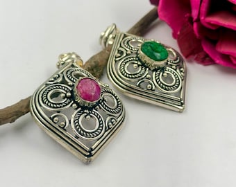 May include: Two silver pendants with intricate filigree metalwork in a diamond shape. One pendant features a round, faceted pink gemstone at its center, while the other pendant contains a round, faceted green gemstone set in the same silver design.
