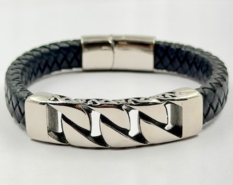 May include: A black braided leather bracelet featuring a polished silver-tone metal centerpiece with a stylized, open-link chain design. The bracelet includes a smooth, rectangular silver-tone metal clasp mechanism at the back for secure closure.