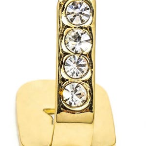 May include: A gold-toned metal ring featuring a vertical bar design adorned with four clear, round, faceted crystals set in a row. The band has a flat, rectangular base section that extends upward into the crystal-encrusted vertical element.