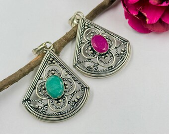 May include: Two fan-shaped silver pendants featuring intricate filigree wirework and beaded detailing. One pendant contains a central oval-cut teal stone, while the other features a central oval-cut magenta stone, both set in polished silver frames.