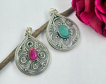 May include: Two teardrop-shaped silver pendants featuring intricate filigree metalwork. One pendant contains a central oval-cut pink gemstone, while the other pendant features a central oval-cut teal gemstone. Both pieces include a small metal bail at the top.