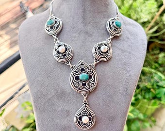 May include: A silver-toned necklace featuring a series of teardrop-shaped links with intricate wirework patterns. The design incorporates two round white pearls and three oval turquoise-colored stones set within the metal filigree structure.