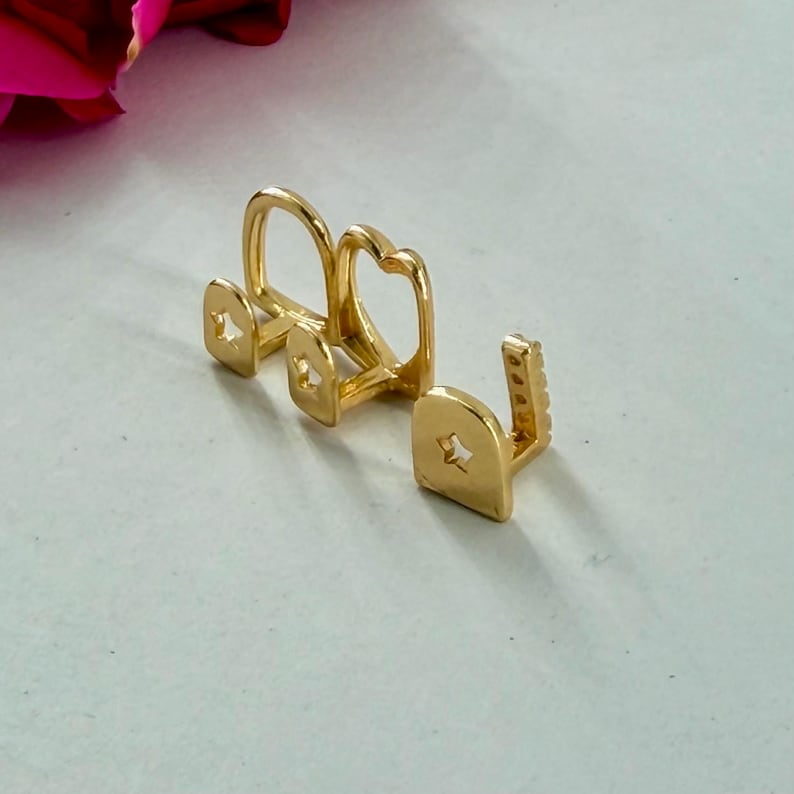 May include: A set of three gold-colored tooth caps, each featuring a small star-shaped cutout on the front surface. The caps are arranged in a row, showing a smooth, polished finish and a distinct U-shaped structure designed to fit over individual teeth.