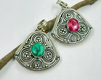 May include: Two silver pendants with intricate filigree metalwork and decorative bead accents. One pendant features a round, textured green stone at the center, while the other contains a smooth, polished round pink stone in the middle.