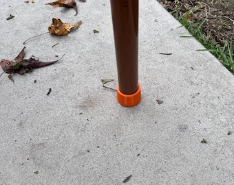 Puede incluir: Un bastón marrón con una punta de goma naranja. El bastón tiene el texto "2XP-POT433" impreso. El bastón está apoyado sobre una superficie de hormigón.