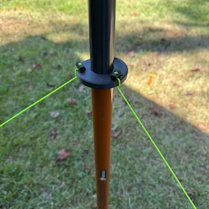 May include: A black and brown pole with a circular black base and bright green guy lines. The pole is set in a grassy area. The pole has a dark brown lower section and a black upper section.