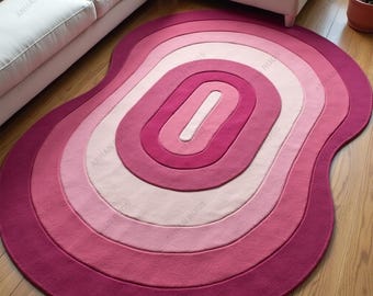 May include: A pink and magenta area rug with an abstract, layered design. The rug features concentric oval shapes in varying shades of pink, creating a gradient effect. The rug is placed on a hardwood floor near a white sofa.