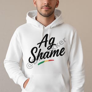 Könnte beinhalten: Weißer Kapuzenpullover mit dem Text "Ag Shame" in schwarzer Schrift. Das Design beinhaltet einen horizontalen Streifen in Rot, Grün und Gelb. Der Pullover hat eine Vordertasche und eine Kapuze mit Kordelzug.