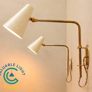 May include: Two wall-mounted lamps featuring brass arms and off-white conical shades with small perforated holes. Each lamp has an adjustable joint and a circular wall plate. A logo with the text VALUABLE LIGHT STORE is visible in the corner.