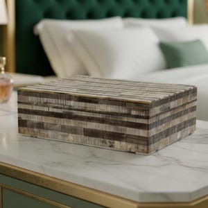 May include: A rectangular storage box featuring a mosaic pattern of horizontal strips in varying shades of brown, gray, and cream. The box has a flat lid and a smooth, multi-toned finish, showcasing a layered, linear design across its exterior surfaces.