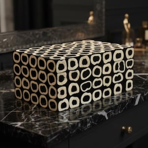 May include: A rectangular storage box featuring a repeating pattern of black and cream-colored organic, rounded shapes. The exterior surface is covered in a dense, grid-like arrangement of these contrasting, irregular circular motifs.