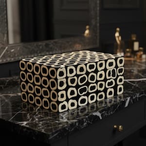 May include: A rectangular black and white decorative box with a repeating pattern of white circles on a black background. The box is placed on a black marble surface, suggesting a luxury item.