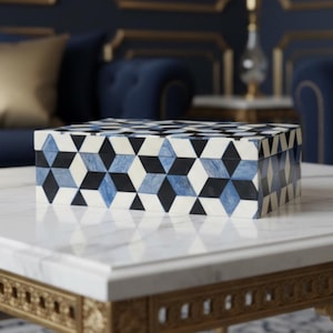 May include: A decorative box with a geometric pattern in black, white, and blue. The box is rectangular and sits on a white marble table. The box's design features a repeating pattern of diamond shapes.
