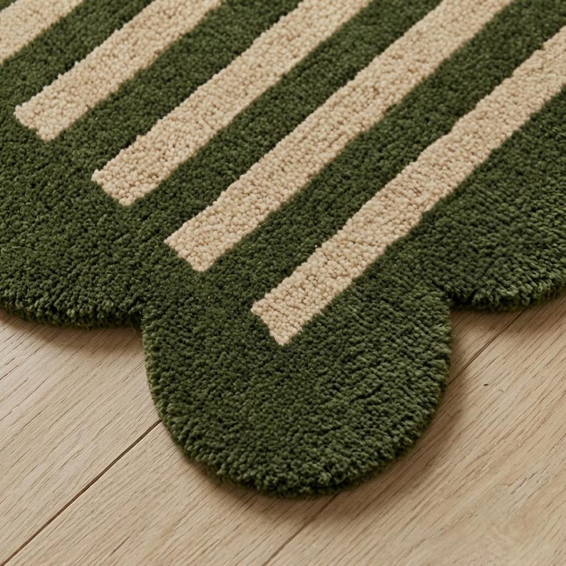 May include: A tufted rug featuring a scalloped edge design with alternating thick stripes in forest green and cream. The textile surface has a dense, textured pile construction that creates a soft appearance across the entire patterned area.