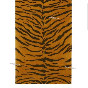 May include: A rectangular area rug featuring a repeating tiger stripe pattern in shades of dark brown and golden orange. The text hometeppich is printed in small white letters across the surface of the rug in three separate locations.