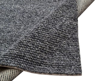 May include: Close-up of a grey rug with a textured, speckled surface. The rug is folded over, revealing a striped underside. The rug's colour is a mix of light and dark grey.