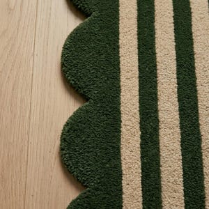 May include: A tufted rug featuring a scalloped edge design with alternating vertical stripes in dark forest green and cream. The textile has a thick, textured pile surface that creates a distinct pattern of parallel lines across the fabric.