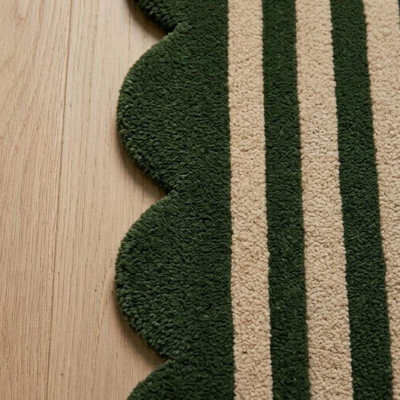 May include: A tufted rug featuring a scalloped edge design with alternating vertical stripes in dark forest green and cream. The textile has a thick, textured pile surface that creates a distinct pattern of parallel lines across the fabric.