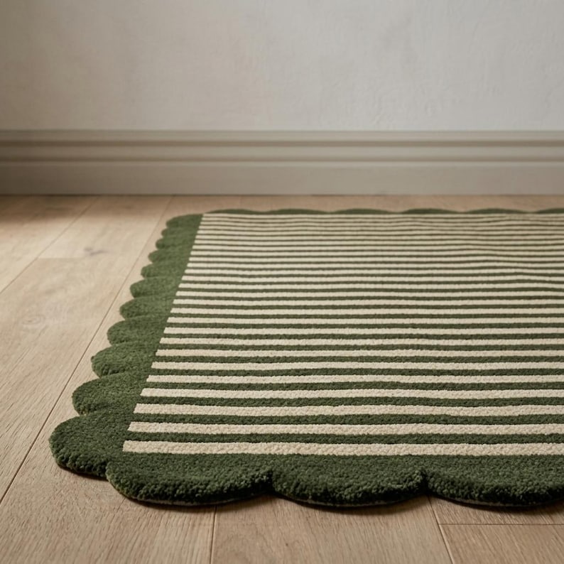 May include: A rectangular rug featuring a pattern of thin, alternating dark olive green and cream-coloured horizontal stripes. The rug is finished with a decorative scalloped edge border in a solid dark olive green, creating a soft, rounded outline.