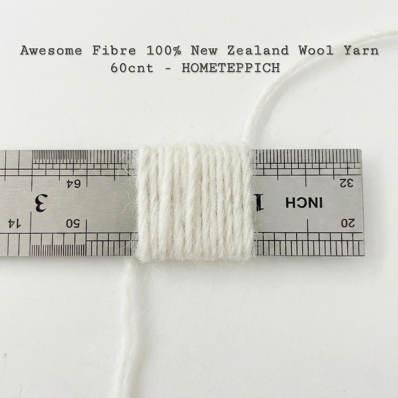 May include: Off-white wool yarn wrapped around a metal ruler, showing a thickness of approximately 1.3 cm. The text Awesome Fibre 100% New Zealand Wool Yarn 60cnt - HOMETEPPICH is printed above the yarn and ruler on a plain white background.