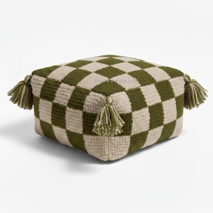 Pode incluir: Um pufe quadrado feito à mão com um padrão xadrez em verde oliva e creme. O pufe tem quatro borlas decorativas, uma em cada canto. O texto "hometeppich" é visível na lateral. Esta peça decorativa é adequada para decoração de interiores.