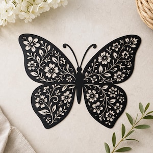 May include: A flat, black butterfly-shaped wall decoration featuring intricate laser-cut details. The wings are filled with a delicate, symmetrical pattern of flowers, leaves, and swirling vines, creating a cutout silhouette design.