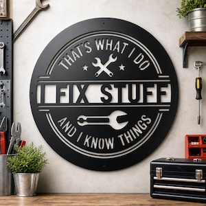 May include: A circular black metal wall sign featuring cut-out text that reads "THAT'S WHAT I DO I FIX STUFF AND I KNOW THINGS" with graphic icons of crossed wrenches and a single wrench centered within the design.