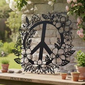 May include: Black metal peace symbol with a floral wreath design. The peace sign is encircled by detailed cut-out flowers and leaves. The text "PEACE BLOOMS" is visible at the bottom. The artwork is displayed outdoors.