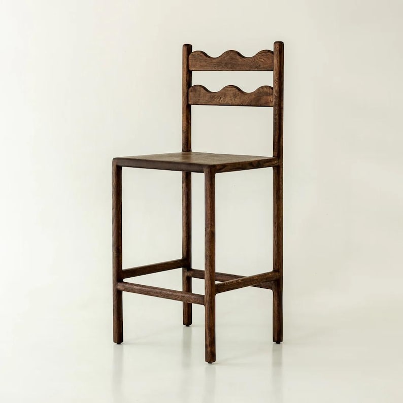 K&ouml;nnte beinhalten: Ein dunkelbrauner Barhocker aus Holz mit quadratischer Sitzfl&auml;che und einer hohen R&uuml;ckenlehne mit zwei horizontalen Streben. Jede Strebe hat ein markantes, wellenf&ouml;rmiges Design. Der Hocker besteht aus vier geraden Beinen, die durch Querstreben verbunden sind.