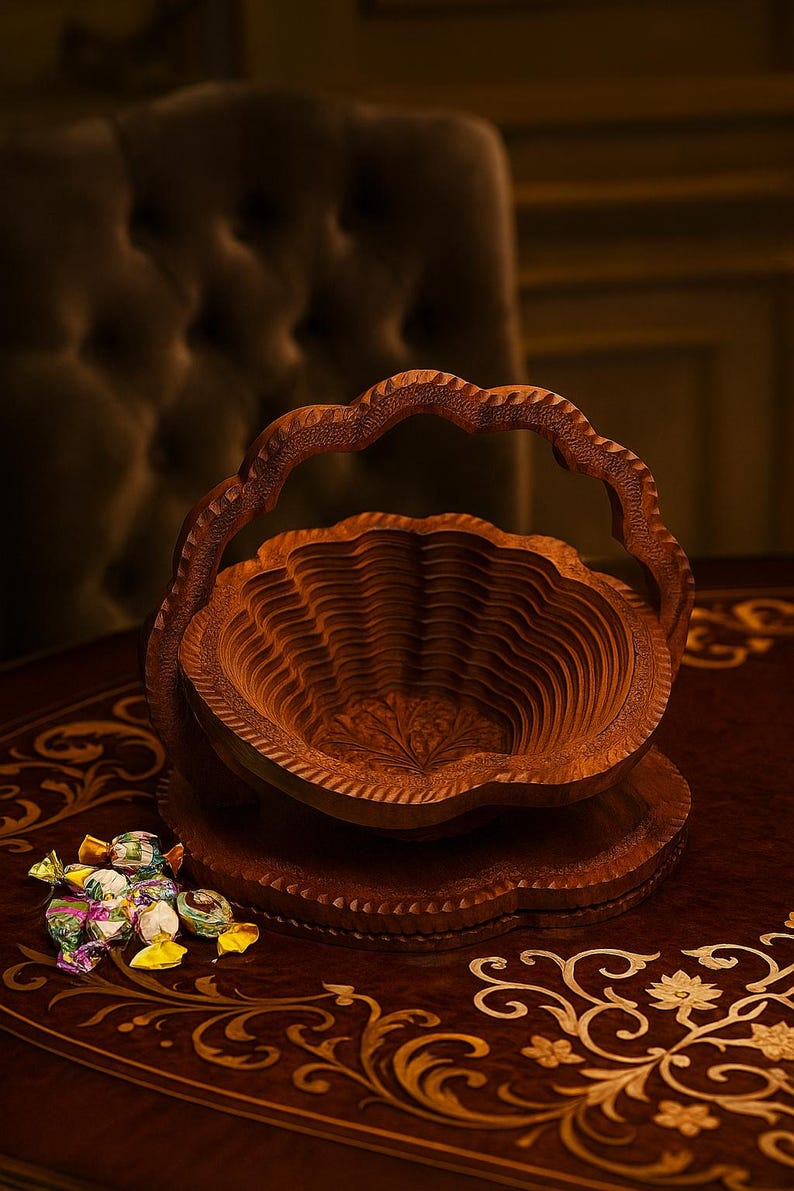 May include: A decorative wooden basket with a handle, carved from a warm brown wood. The basket has a layered design and sits on a matching base. A small pile of wrapped candies rests nearby. The basket is on a table with ornate gold detailing.