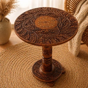 May include: A round, dark brown wooden side table with intricate floral carvings. The table features a central inlaid design and a pedestal base. The table is approximately 24 inches in diameter and 28 inches tall.