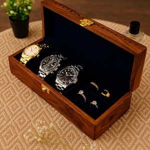 May include: A wooden watch and jewelry box with a dark blue interior. The box contains three watches with silver and gold bands, and four rings. The box is made of dark wood and has a gold clasp.
