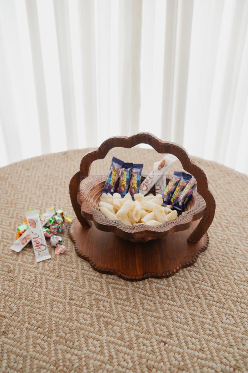 May include: A decorative wooden serving bowl filled with snacks and candy. The bowl has a unique scalloped edge design and is filled with white snacks and wrapped candies. Several snack bars are also included.